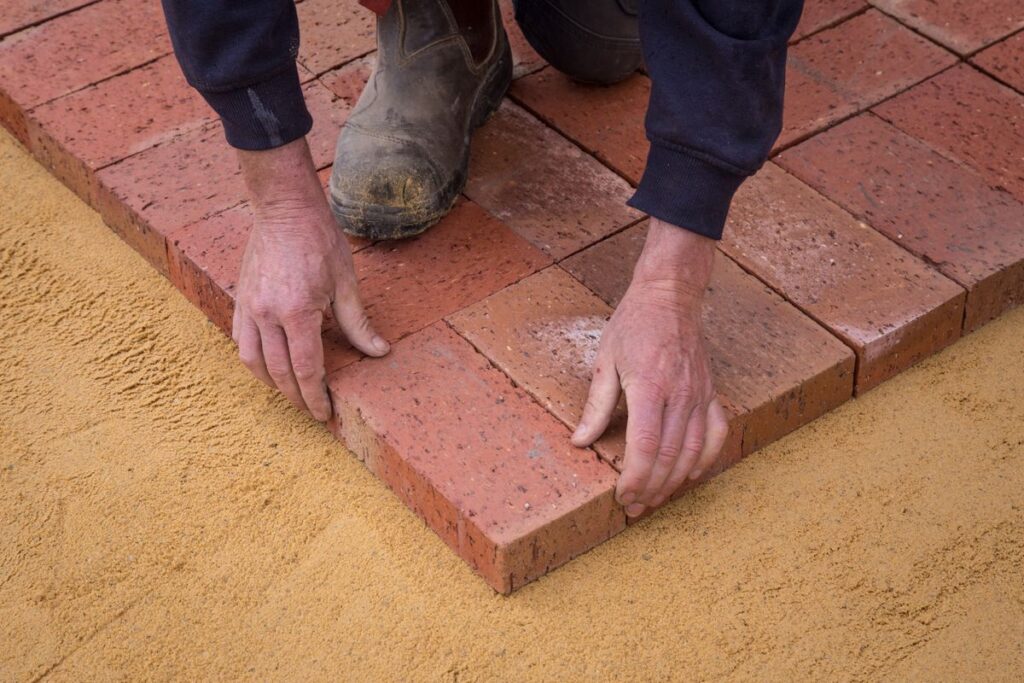 Worker laying pavers level on a compacted sand base