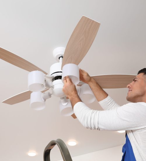 Electrician changing light bulb in ceiling fan indoors