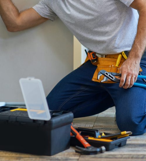 Cropped shot of professional repairman using pipe wrench and other tools while examining and fixing sink pipe in the kitchen. Repair service and plumbing concept. Horizontal shot